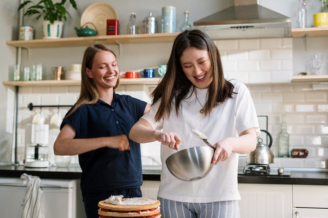 Two women laughing as they mix ingredients from a family-friendly recipe from a blog.