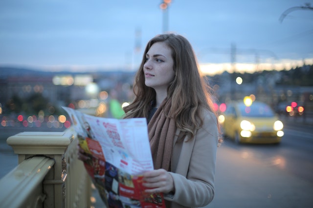 A woman on a bridge holding a map planning her travel itinerary.