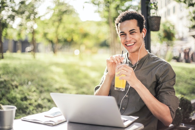 A man with a laptop smiling and holding juice as he reads a casual mens lifestyle blog.